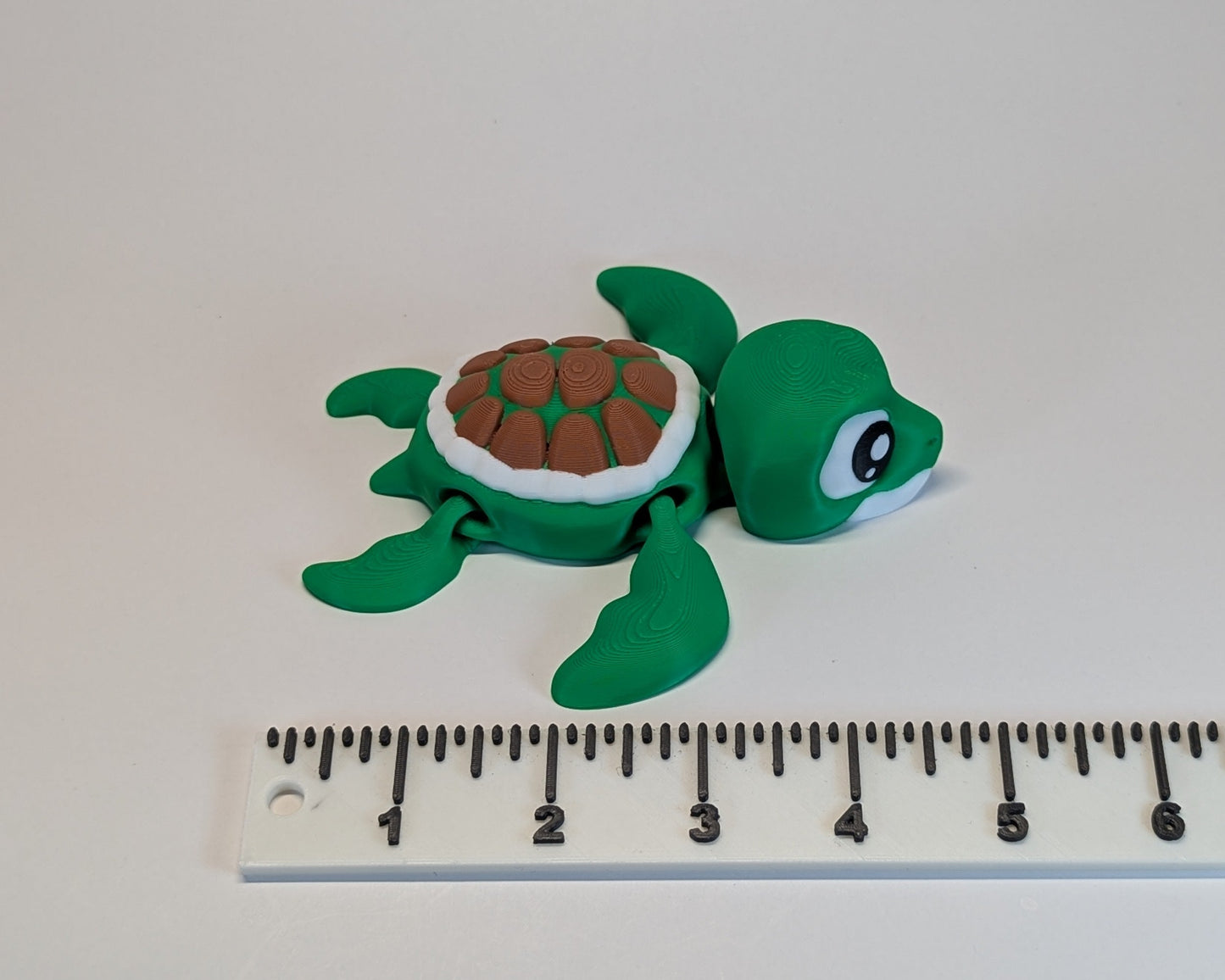 Green turtle figurine next to a ruler on a white background