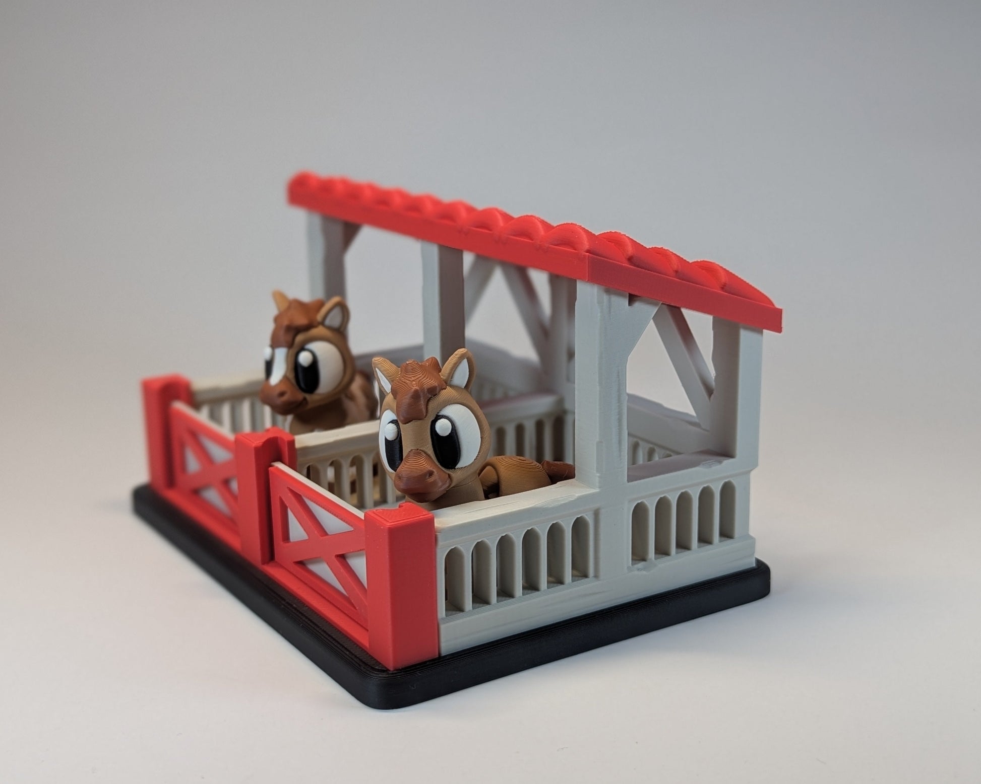 Toy horse stable with two toy horses inside on a gray background