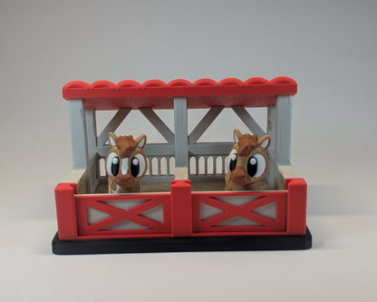Two toy horses in a red and gray stable on a light gray background