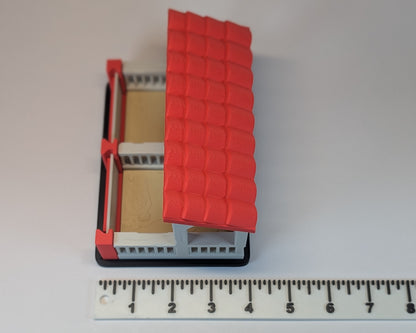 Tiny Habitat Stable with a red roof next to a ruler on a white background