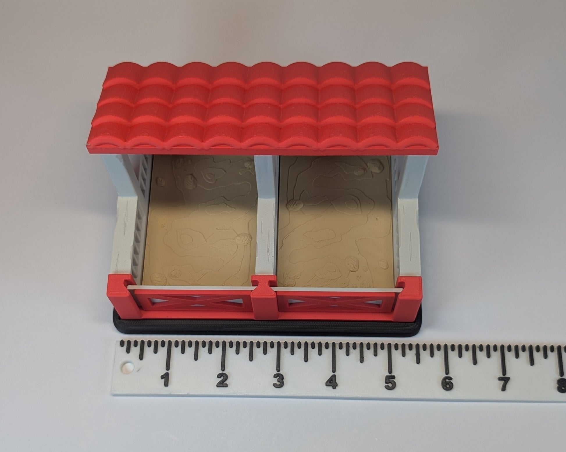 Tiny Habitat Stable with a red roof on a white background with a ruler for scale.