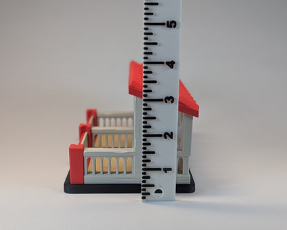 Tiny Habitat Stable with red roof and white base next to a ruler for scale on a gray background