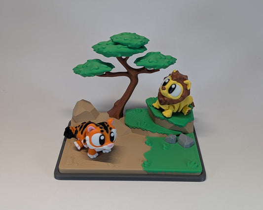 Toy lion and tiger figurines on a miniature landscape with a tree and rocks.